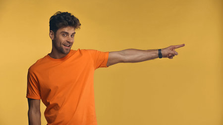 happy man pointing away with finger isolated on yellow