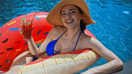 happy woman holding cocktail and lying on swim ring in pool