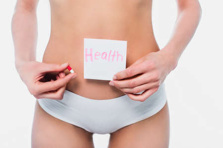 Cropped view of woman in panties holding card with health lettering and pill isolated on whiteの写真素材
