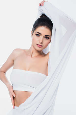 Brunette woman in bra looking at camera while holding cloth isolated on whiteの写真素材
