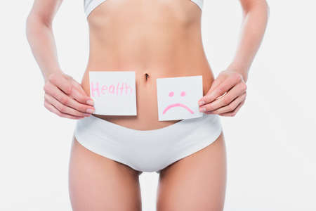 Cropped view of woman in underwear holding cards with health lettering and sad emoticon isolated on whiteの写真素材