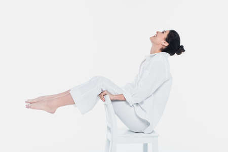 Side view of woman in white clothes smiling on chair isolated on whiteの写真素材