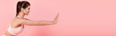 Side view of fit sportswoman exercising isolated on pink, bannerの写真素材