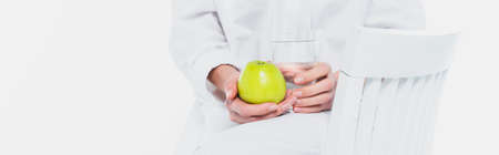 Cropped view of water and apple in hands of woman on chair isolated on white, bannerの写真素材