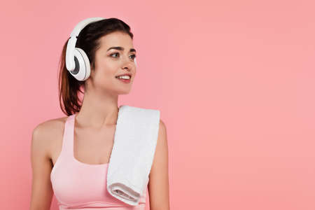 Positive sportswoman in headphones with towel isolated on pinkの写真素材