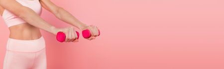 Cropped view of dumbbells in hands of fit sportswoman blurred isolated on pink, bannerの写真素材