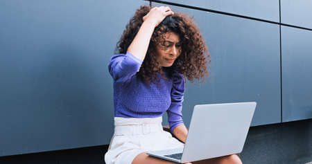 stressed freelancer adjusting hair while using laptop outsideの写真素材