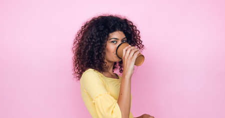 curly young woman drinking coffee to go isolated on pinkの写真素材