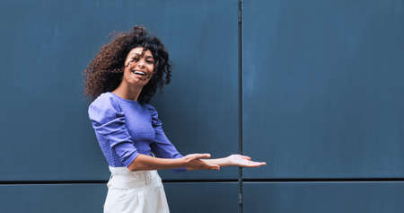 cheerful young woman pointing with hands near building outsideの写真素材