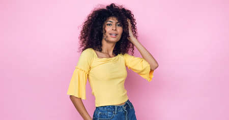 young model posing and adjusting curly hair isolated on pinkの写真素材