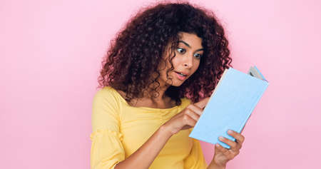 excited young woman reading book isolated on pinkの写真素材