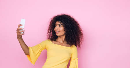 happy young woman taking selfie on smartphone isolated on pinkの写真素材