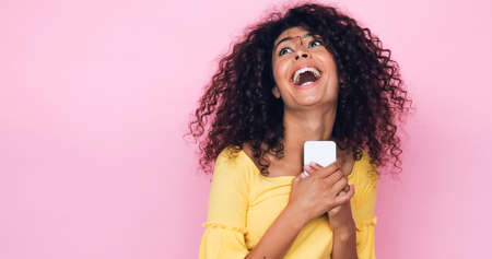 amazed young woman holding mobile phone isolated on pinkの写真素材