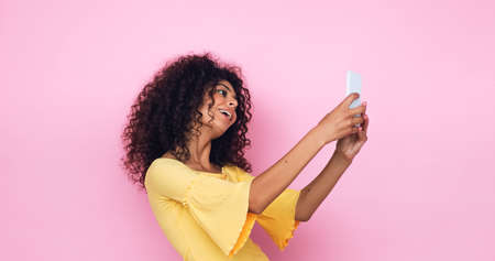 curly young woman taking selfie on smartphone isolated on pinkの写真素材