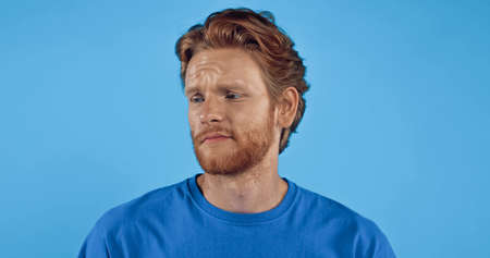 bearded and redhead man in t-shirt looking away isolated on blueの写真素材
