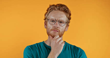 pensive redhead man in glasses thinking isolated on yellowの写真素材