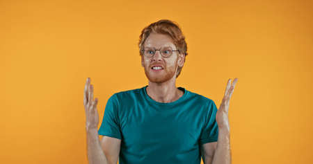 angry redhead man in glasses gesturing isolated on yellowの写真素材
