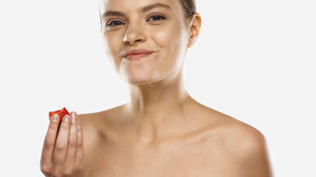 young woman with bare shoulders eating strawberry and smiling isolated on whiteの写真素材