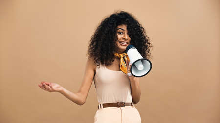 Cheerful hispanic woman holding loudspeaker isolated on beigeの写真素材