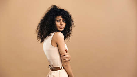 Curly hispanic woman looking at camera isolated on beigeの写真素材