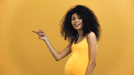 Pregnant hispanic woman pointing with finger isolated on yellowの写真素材