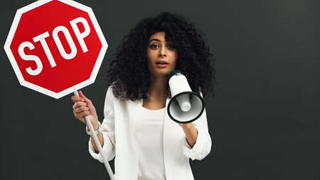 hispanic woman holding stop signboard and loudspeaker isolated on blackの写真素材