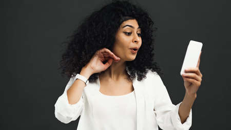 Excited hispanic woman using smartphone on blurred foreground isolated on blackの写真素材