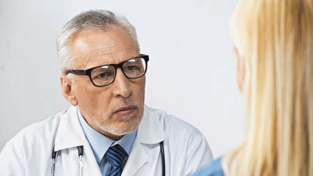 doctor in eyeglasses listening to woman during appointment in clinic, blurred foregroundの写真素材