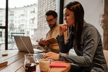 brunette freelancer using laptop near man in cafeの写真素材