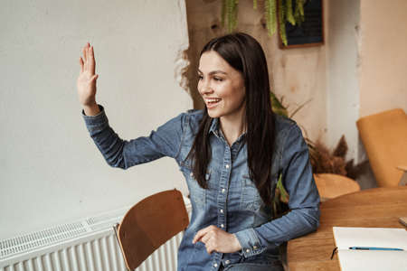 cheerful woman waving hand while sitting in cafeの写真素材