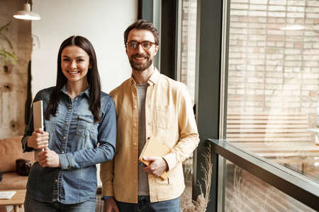 cheerful woman holding laptop near man in glasses with notebookの写真素材