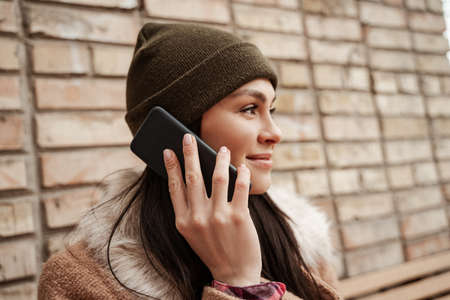 brunette woman in beanie hat smiling while talking on smartphone