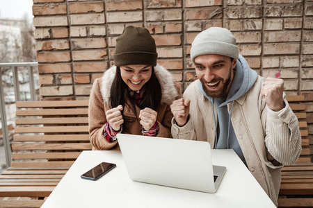amazed freelancers in beanie hats looking at laptop on tableの写真素材