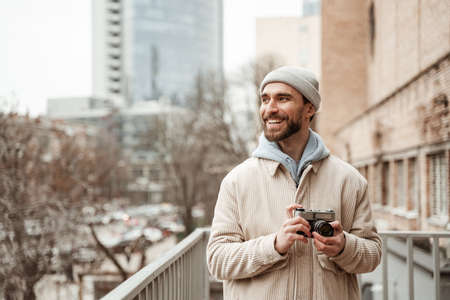 bearded man in beanie hat and jacket smiling while holding retro cameraの写真素材