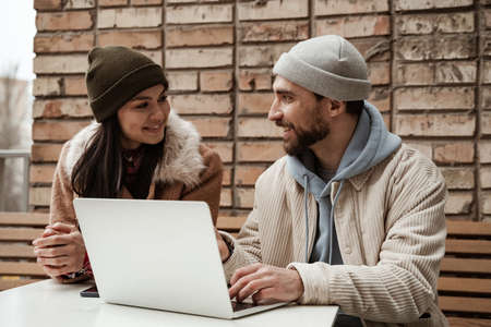 cheerful freelancer in beanie hats looking at each other near laptopの写真素材