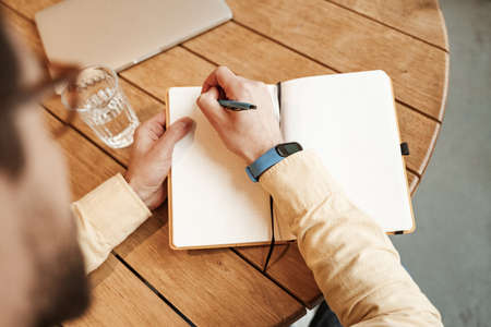 high angle view of freelancer with smart watch on hand writing in notebookの写真素材
