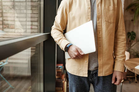 cropped view of freelancer holding laptop while standing near windowの写真素材