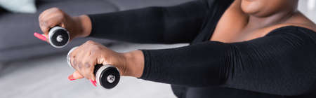 partial view of african american plus size woman in sportswear exercising with dumbbells, bannerの写真素材
