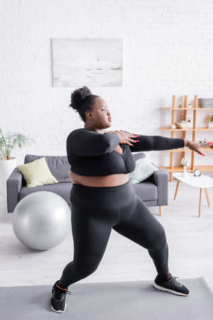 full length of african american plus size woman in sportswear exercising in living roomの写真素材