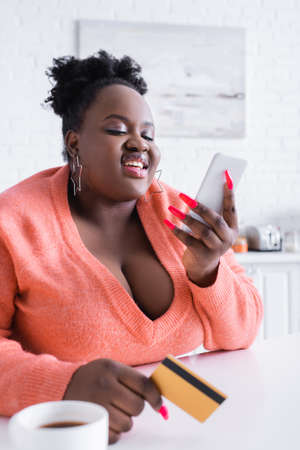 smiling african american plus size woman holding credit card and smartphoneの写真素材