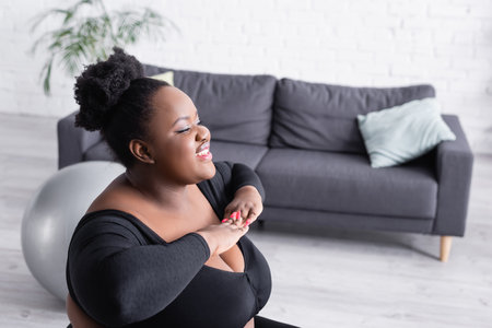 smiling african american plus size woman in sportswear exercising in living roomの写真素材