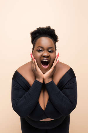 amazed african american plus size woman looking at camera isolated on beigeの写真素材