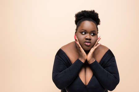 african american plus size woman looking away isolated on beigeの写真素材