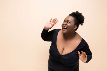 excited african american plus size woman looking away isolated on beigeの写真素材