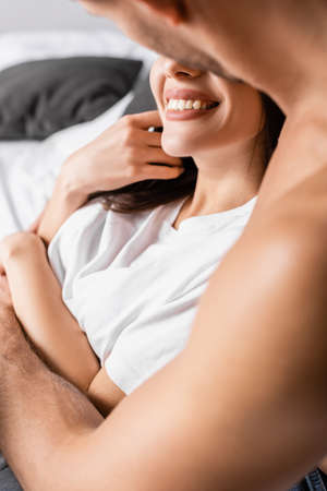 Muscular man on blurred foreground hugging smiling woman on bed