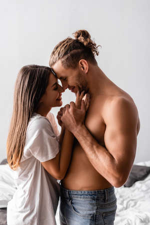 Side view of smiling woman touching face of sexy boyfriend at homeの写真素材