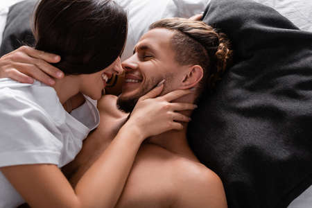 Young woman in t-shirt kissing smiling boyfriend on bedの写真素材