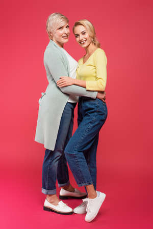 full length view of cheerful mother and daughter in stylish clothes embracing on pinkの写真素材