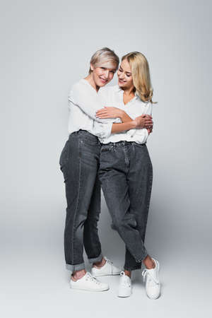full length view of mature woman embracing young, stylish daughter on grayの写真素材