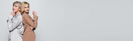 fashionable mother and daughter looking at camera while standing back to back isolated on gray, bannerの写真素材